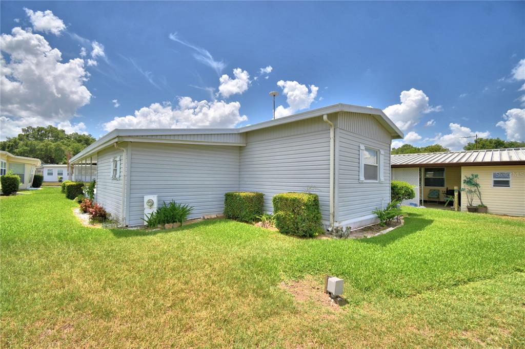 A light gray mobile home exterior with a lawn and bushes under a blue sky — 118 PARADISE LANE, AUBURNDALE, FL