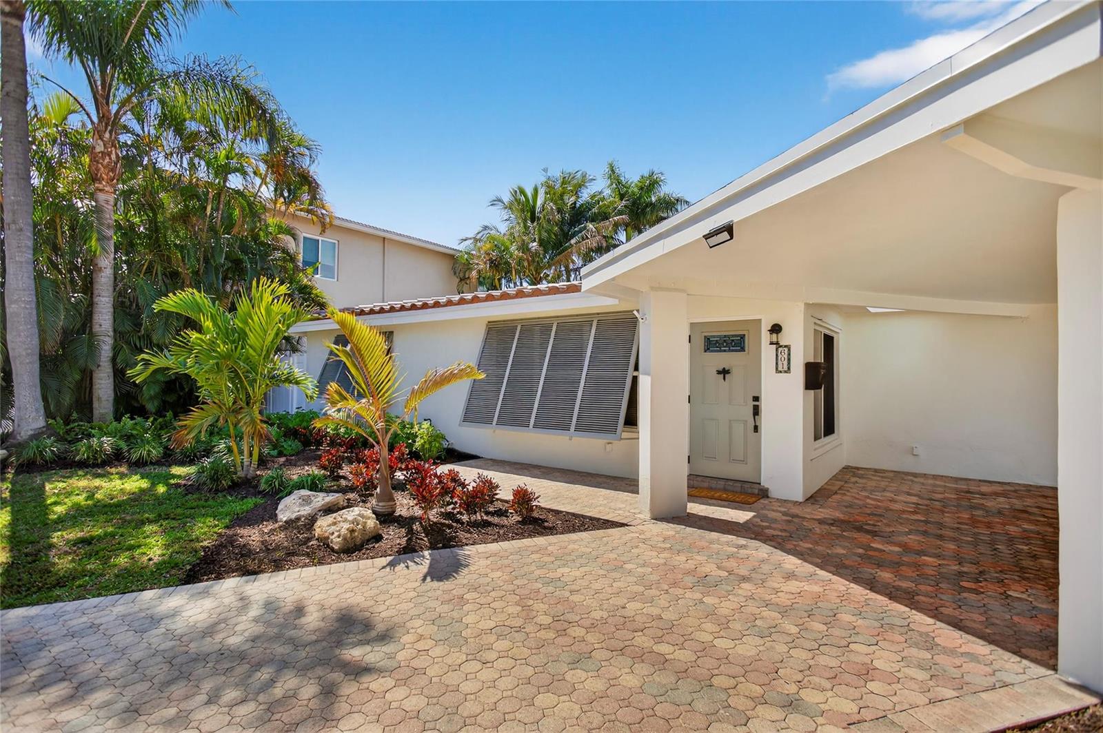 A white house exterior features a brick paver driveway, a covered entryway, and tropical landscaping — 601 SE 5th Terrace, Pompano Beach FL 33060, POMPANO BEACH, FL