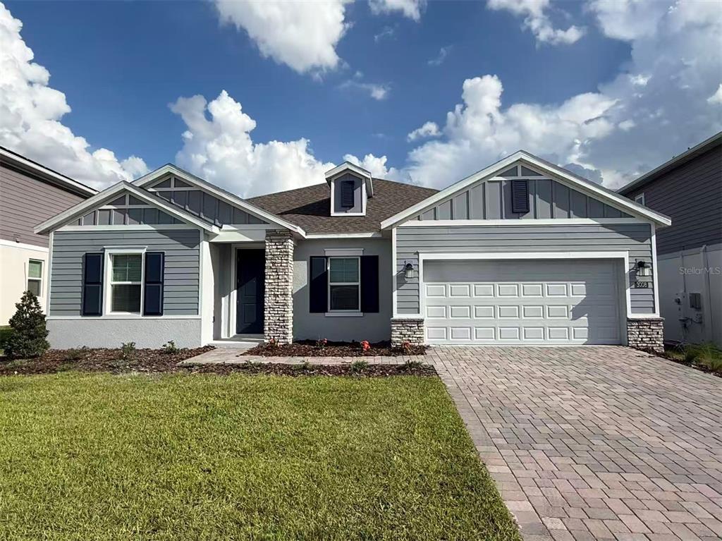A single-story house with gray siding, stone accents, and a paved driveway under a cloudy sky — 3008 ELLA WAY, ST CLOUD, FL