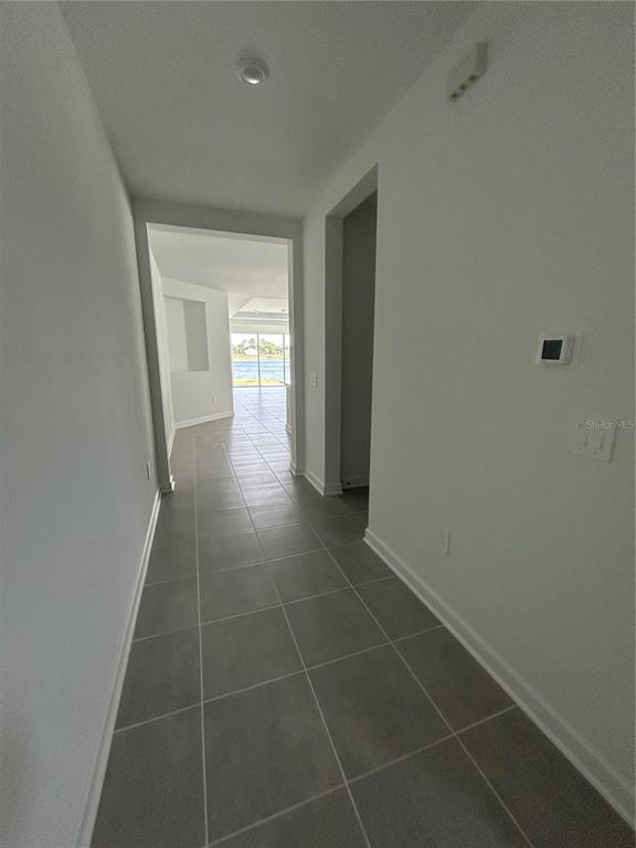 A hallway with gray tile flooring leads toward a bright living area with water views — 3008 ELLA WAY, ST CLOUD, FL