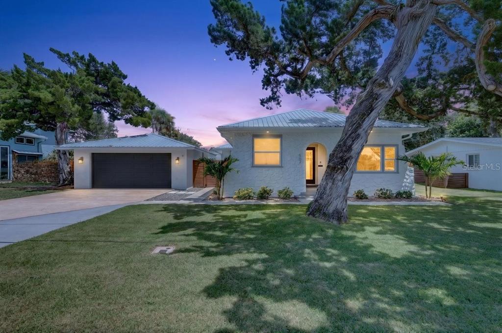 A single-story house with a white stucco exterior, metal roof, and attached garage at dusk — 507 GOODWIN AVENUE, NEW SMYRNA BEACH, FL