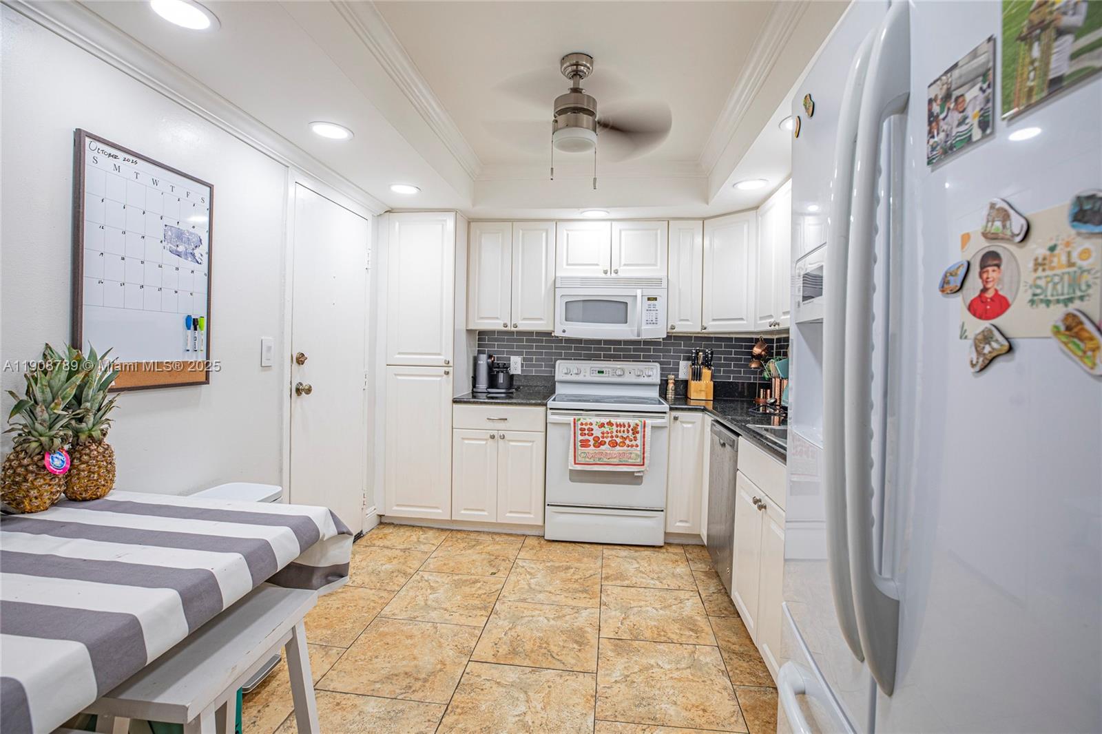 A kitchen features white cabinetry, dark countertops, a tiled backsplash, and a ceiling fan — 437 Golden Isles Dr # C, Hallandale Beach FL 33009, HALLANDALE BEACH, FL