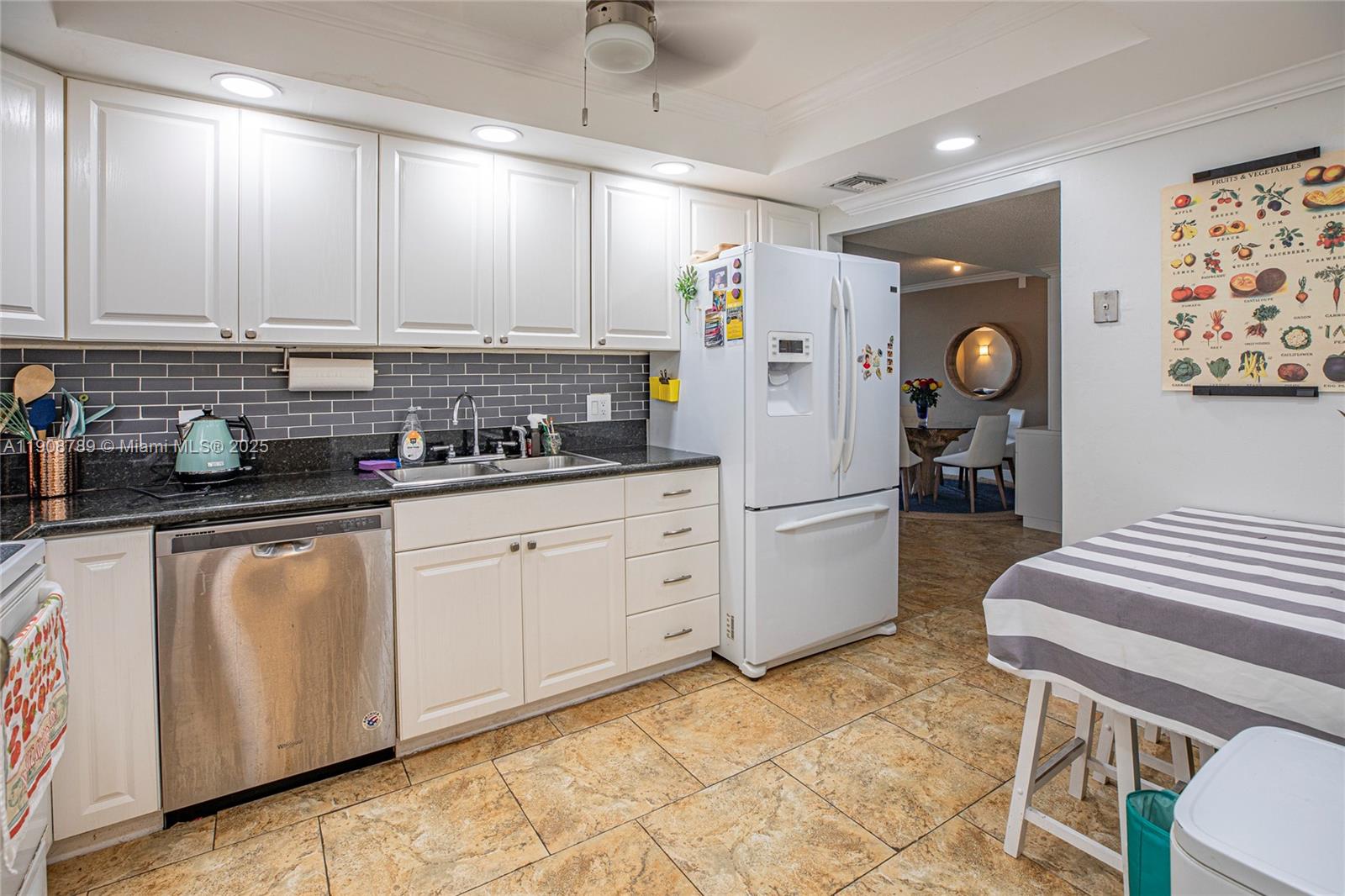A kitchen features white cabinets, stainless steel appliances, dark countertops, and a gray tiled backsplash — 437 Golden Isles Dr # C, Hallandale Beach FL 33009, HALLANDALE BEACH, FL