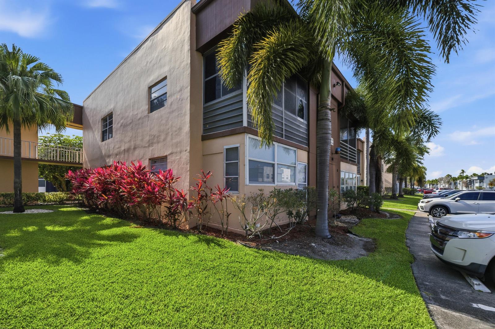 A two-story apartment building with tan stucco walls, screened balconies, and palm trees — 519 Burgundy K, Delray Beach FL 33484, DELRAY BEACH, FL