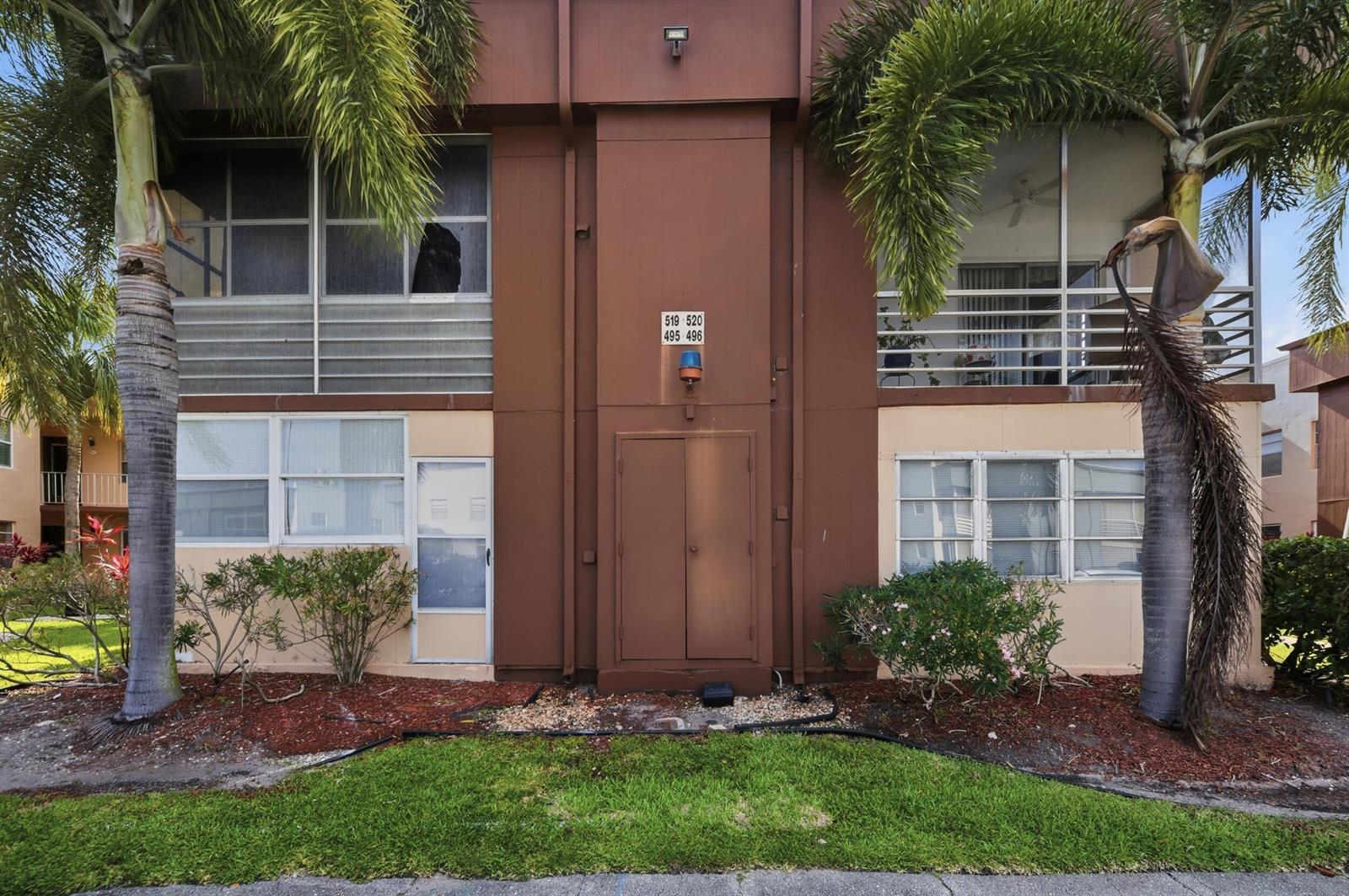 The exterior of a two-story apartment building features brown siding, palm trees, and unit numbers — 519 Burgundy K, Delray Beach FL 33484, DELRAY BEACH, FL