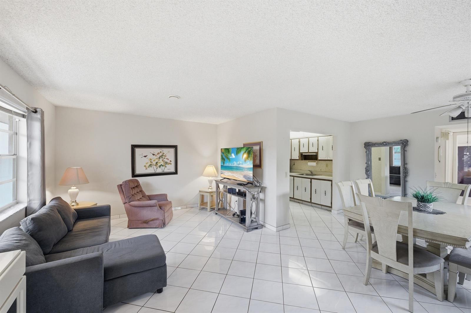 A living and dining area with white tile floors, a grey sectional, and an open kitchen — 519 Burgundy K, Delray Beach FL 33484, DELRAY BEACH, FL