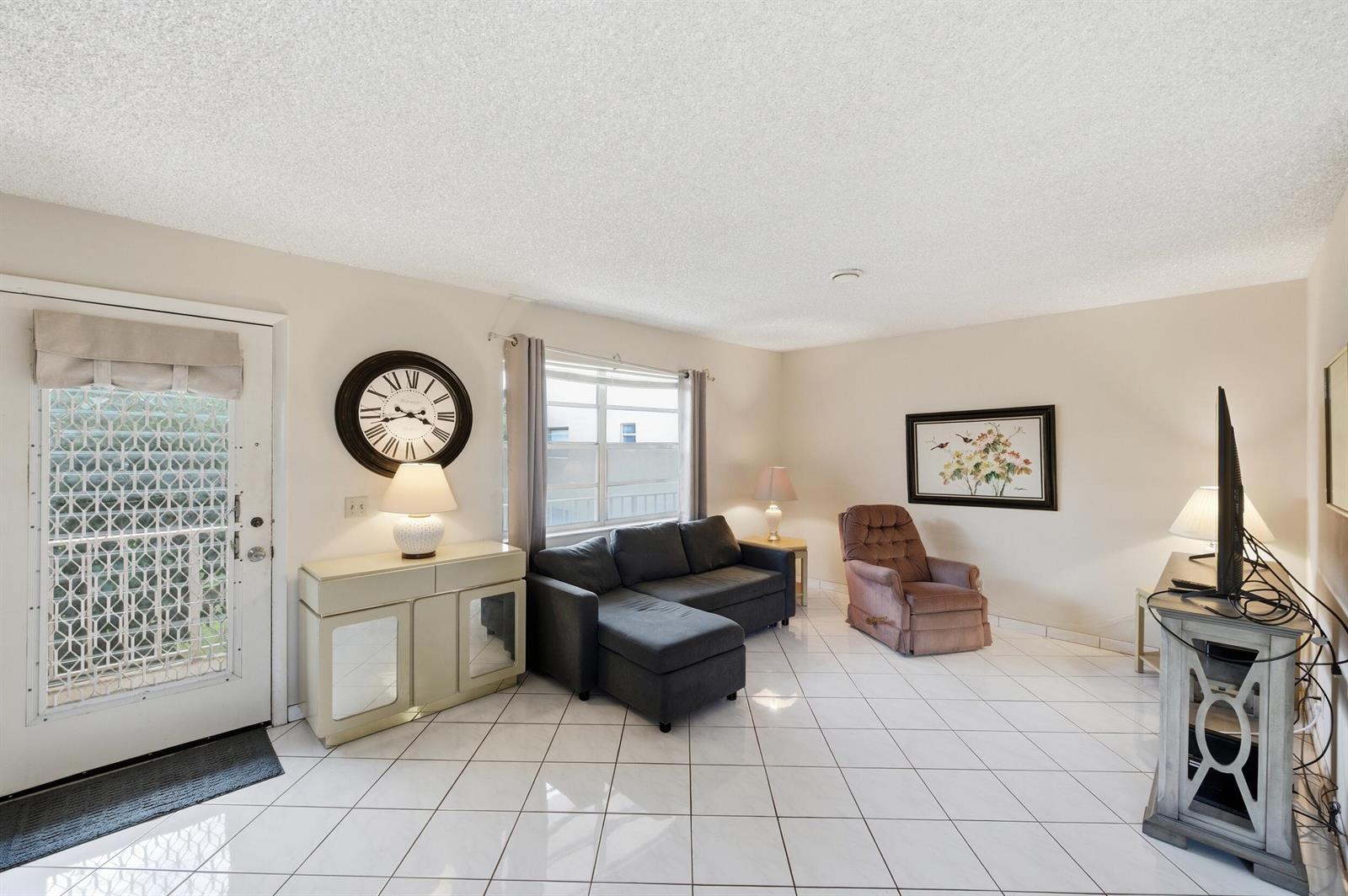 A living room with white tile floors, a dark sectional sofa, and a recliner — 519 Burgundy K, Delray Beach FL 33484, DELRAY BEACH, FL
