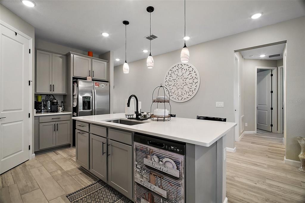 A modern kitchen features gray cabinets, a white quartz island with a sink, and pendant lighting — 2451 SPRING BREEZE DRIVE, LEESBURG, FL