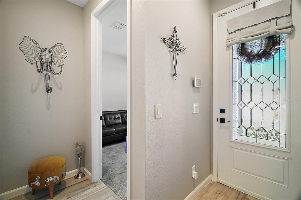 An entryway with a white door, a metal elephant wall decoration, and a small ottoman — 2451 SPRING BREEZE DRIVE, LEESBURG, FL