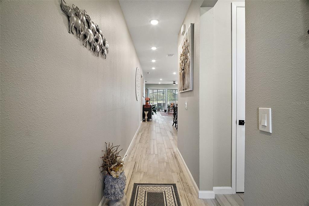 A hallway with light-colored wood-look tile flooring leads toward an open living area — 2451 SPRING BREEZE DRIVE, LEESBURG, FL