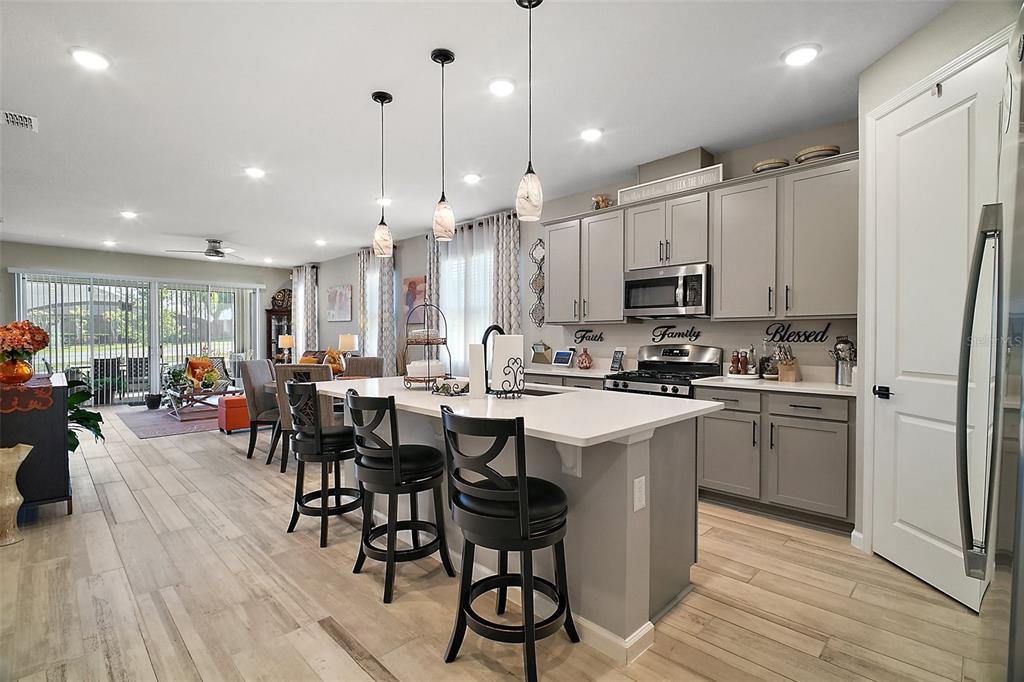A kitchen with gray cabinets, a white island, and bar stools, opening to a living area — 2451 SPRING BREEZE DRIVE, LEESBURG, FL