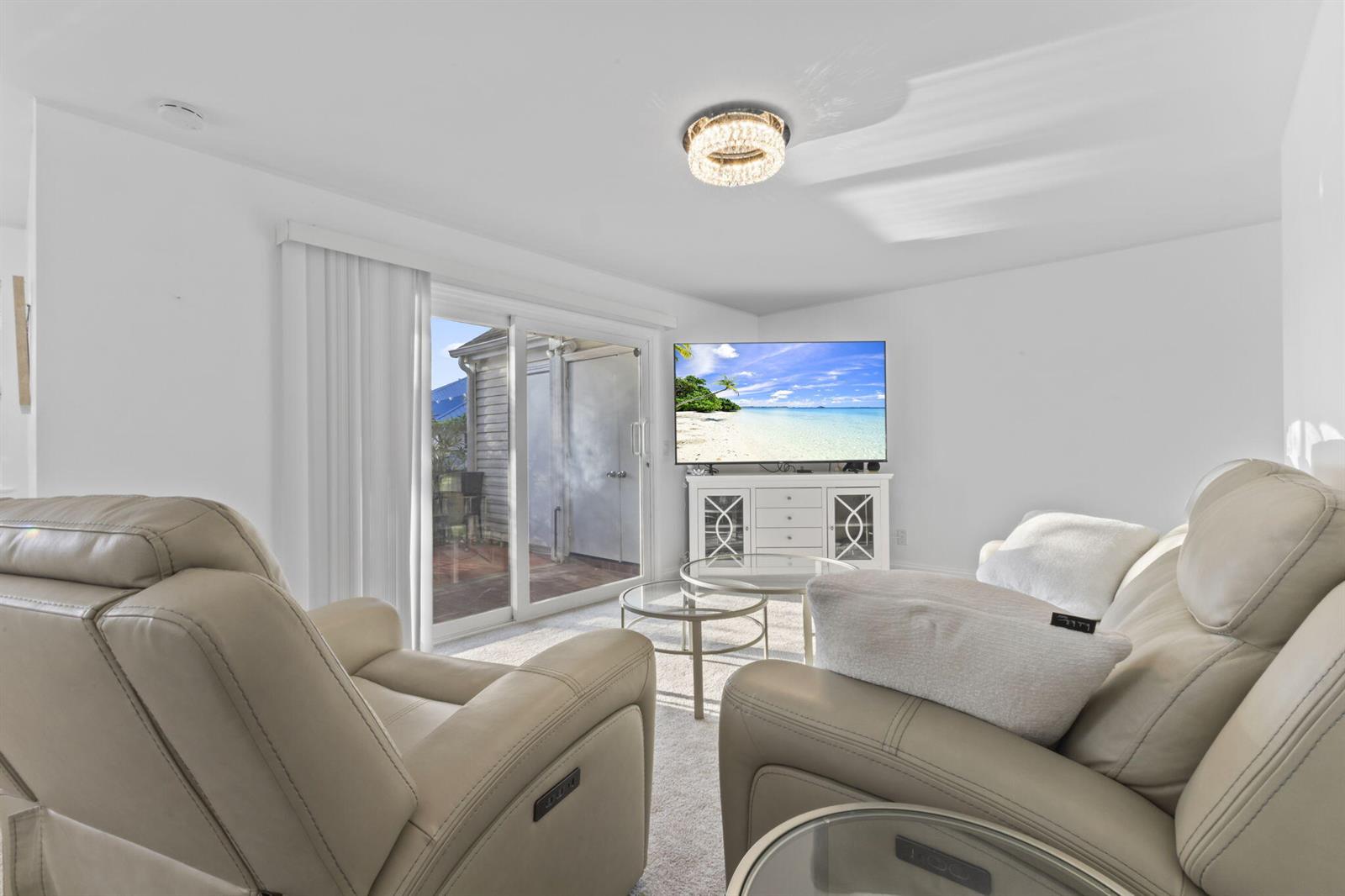 A living room features beige leather recliners, a glass coffee table, and a sliding glass door — 1907 Aynsley Way # 321, Vero Beach FL 32966, VERO BEACH, FL