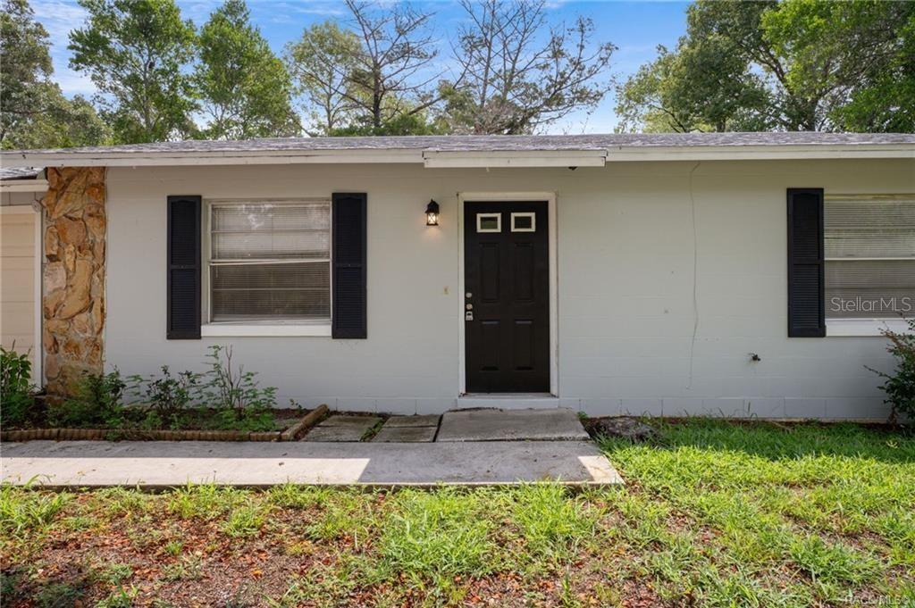 A single-story house exterior features a black front door, white siding, and stone accents — 63 N CROFT AVENUE, INVERNESS, FL