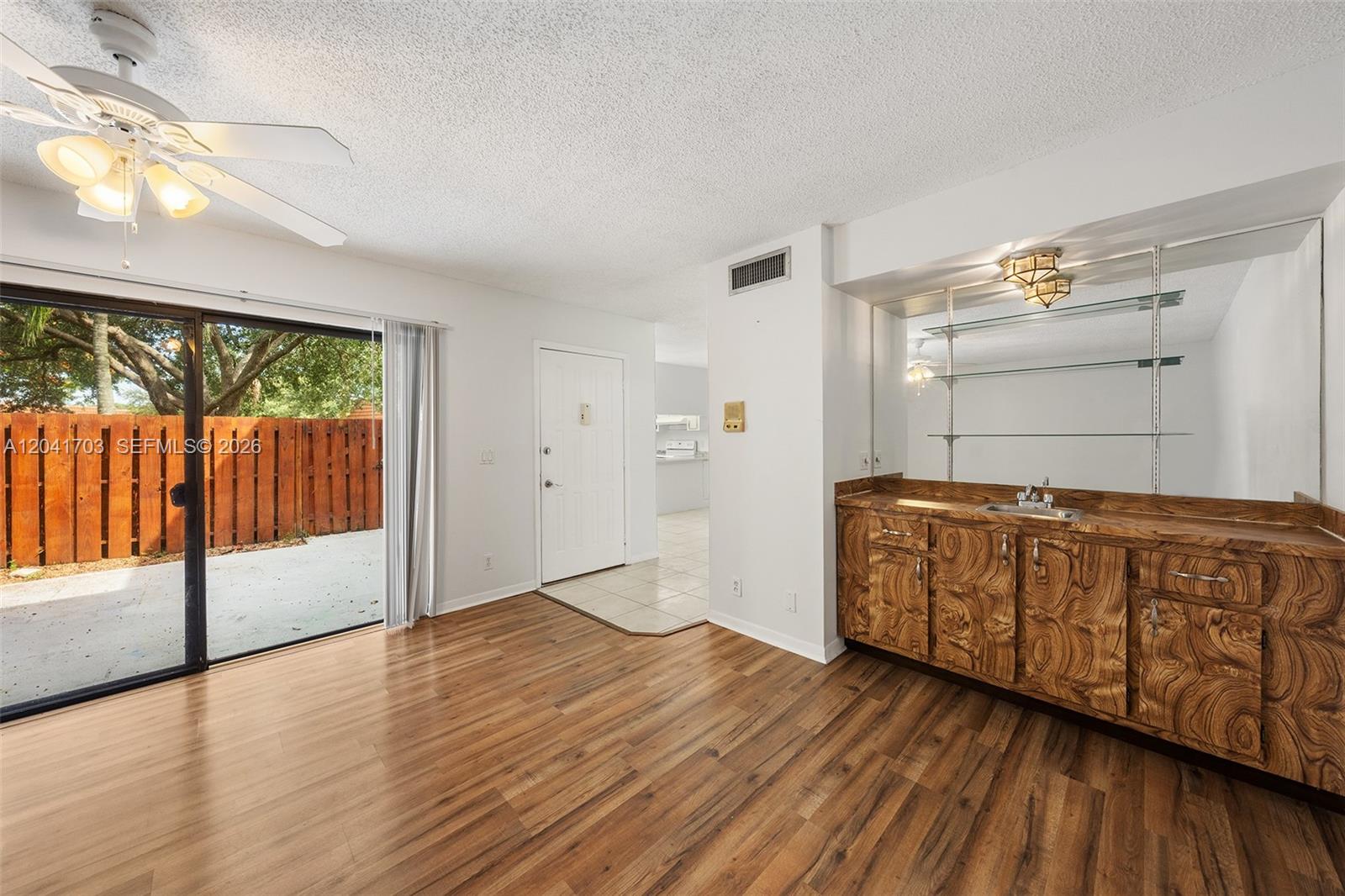 A living room features wood-look flooring, a wet bar with mirrored shelving, and sliding glass doors — 3118 Spanish Wells Dr # C, Delray Beach FL 33445, DELRAY BEACH, FL