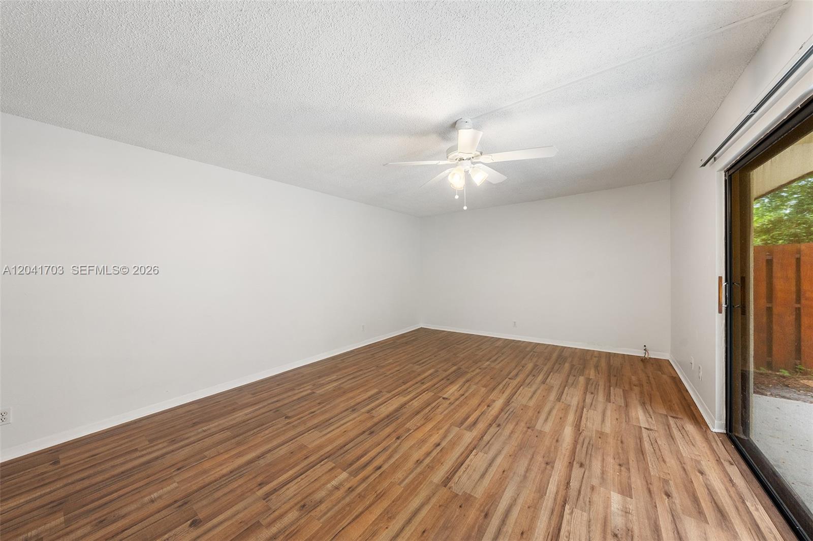 An empty room features white walls, wood-look flooring, a ceiling fan, and a sliding glass door — 3118 Spanish Wells Dr # C, Delray Beach FL 33445, DELRAY BEACH, FL