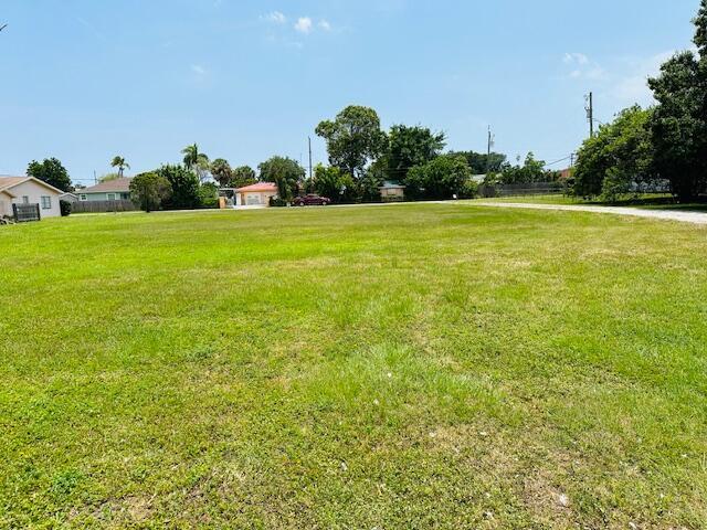 A wide, grassy vacant lot is surrounded by residential houses and trees under a blue sky — 3421 Helena Drive, Lake Worth FL 33461, LAKE WORTH, FL