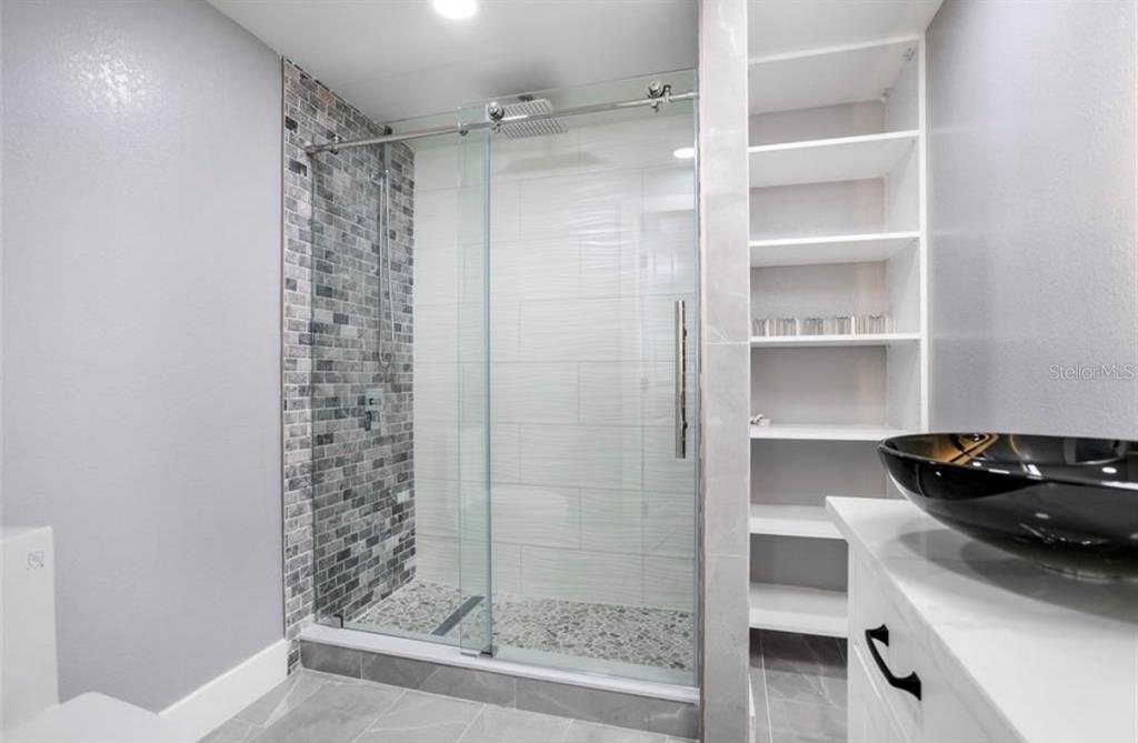 A modern bathroom features a glass-enclosed walk-in shower with pebble flooring and built-in shelving — 8907 N BOULEVARD, TAMPA, FL