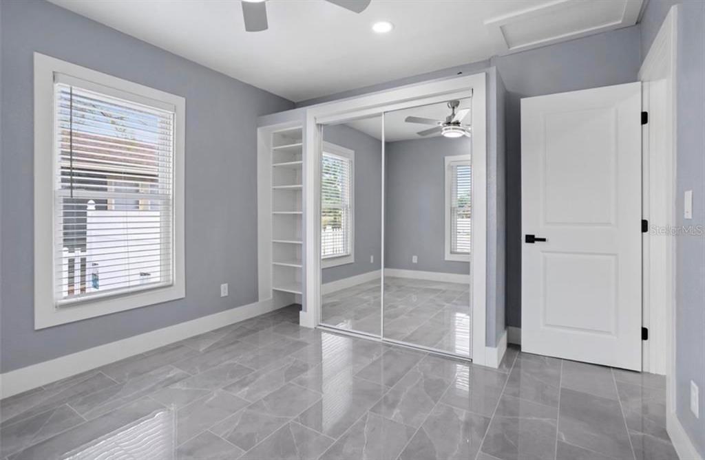A bedroom with gray walls, gray tile flooring, built-in shelving, and mirrored sliding closet doors — 8907 N BOULEVARD, TAMPA, FL