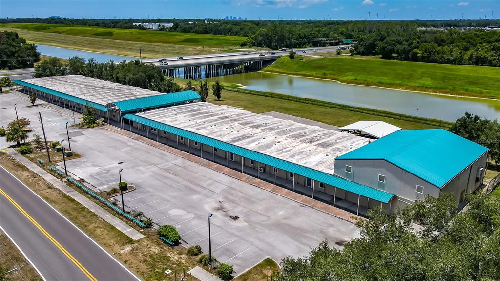 An aerial view shows a long building with a teal roof, a gazebo, and a basketball court — 11734 JEFFERSON ROAD, THONOTOSASSA, FL