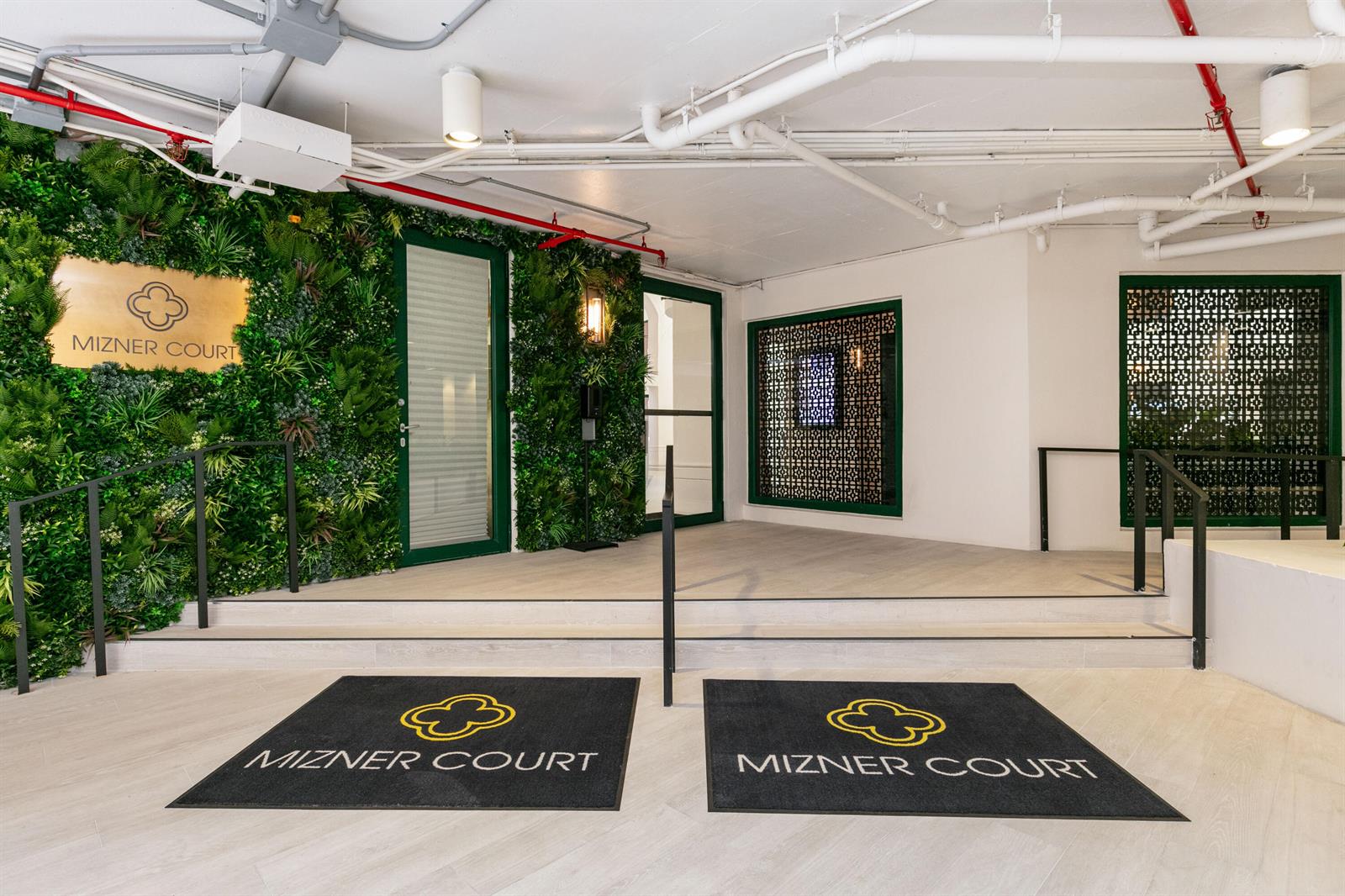A building entrance features two Mizner Court floor mats, a green wall, and white ceilings — 120 SE 5th Avenue E # 127, Boca Raton FL 33432, BOCA RATON, FL