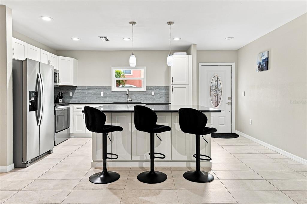A modern kitchen features white cabinets, a black island with three stools, and tile flooring — 608 SAINT JUDES DRIVE, LONGBOAT KEY, FL