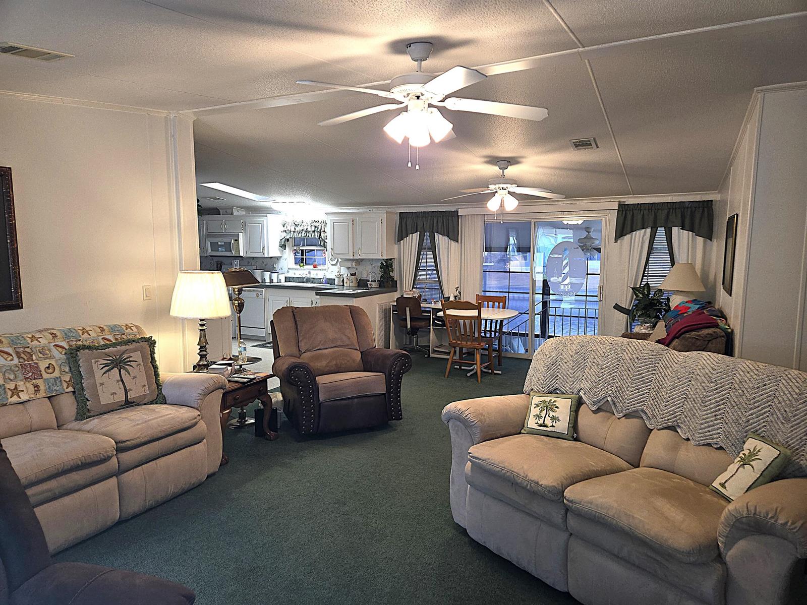 A living room with green carpet, two beige sofas, a recliner, and an open kitchen — 2425 SE 31st Street, Okeechobee FL 34974, OKEECHOBEE, FL