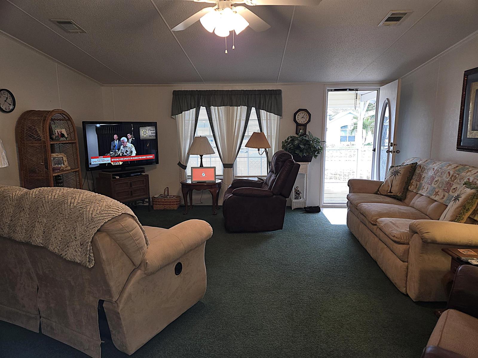 A living room features green carpeting, a television, a recliner, and a sofa near an open door — 2425 SE 31st Street, Okeechobee FL 34974, OKEECHOBEE, FL