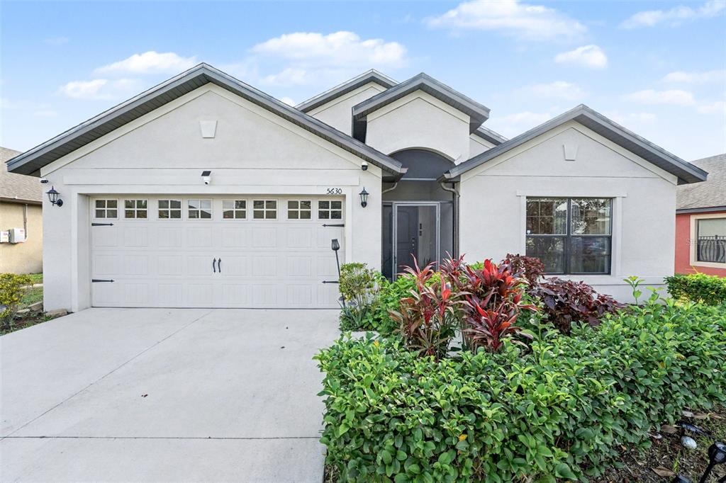 A single-story house with a two-car garage, light-colored stucco exterior, and a landscaped front yard — 5630 ELSINORE WAY, LAKELAND, FL