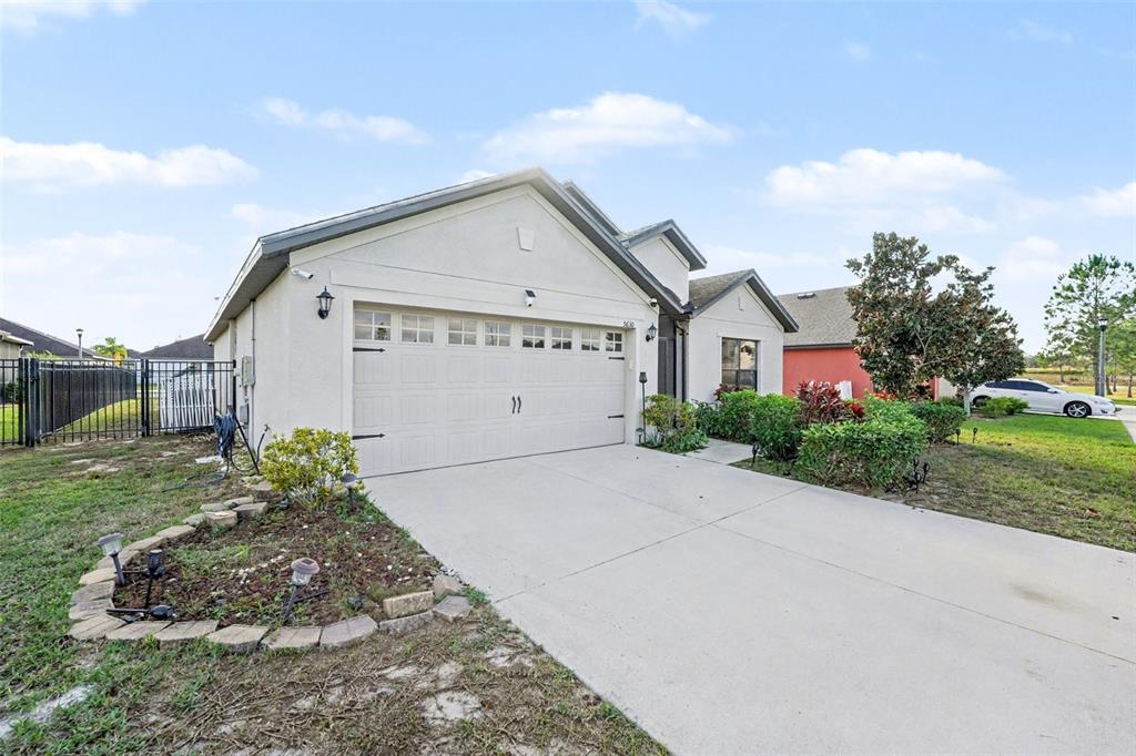 A single-story house with a beige stucco exterior, a two-car garage, and a concrete driveway — 5630 ELSINORE WAY, LAKELAND, FL