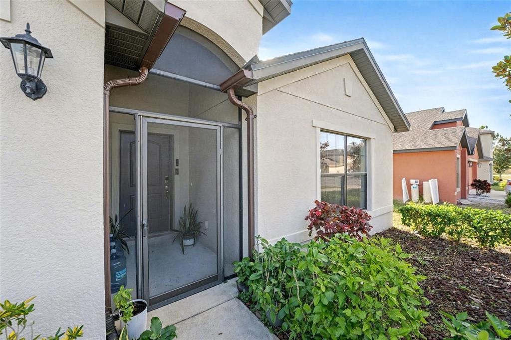 The exterior of a house features a screened front entryway, a window, and landscaping — 5630 ELSINORE WAY, LAKELAND, FL
