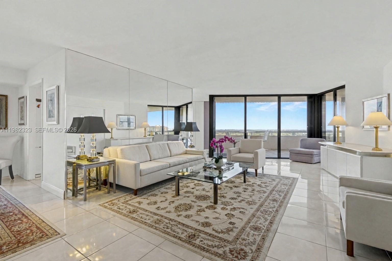 A bright living room features a mirrored wall, white tile floors, and a balcony view — 2000 Towerside Ter, Miami FL 33138, MIAMI, FL