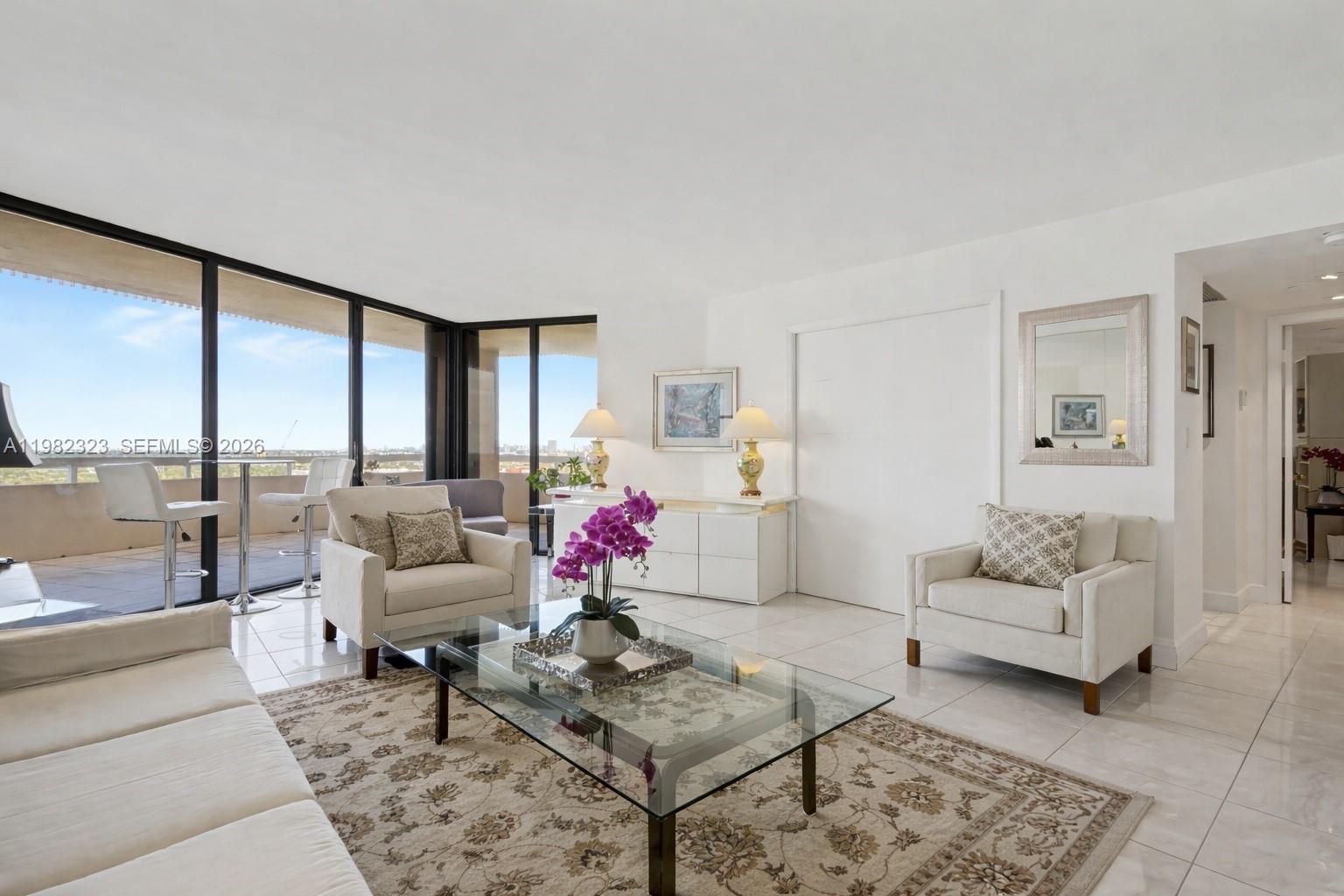 A bright living room features white tile floors, a glass coffee table, and balcony access — 2000 Towerside Ter, Miami FL 33138, MIAMI, FL