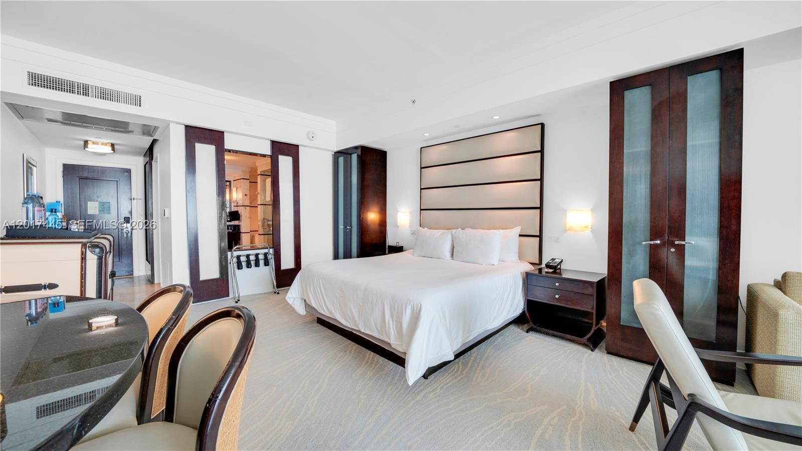 A hotel room features a king bed, dark wood furniture, and a small dining area — 4391 Collins Ave # 1903, Miami Beach FL 33140, MIAMI BEACH, FL