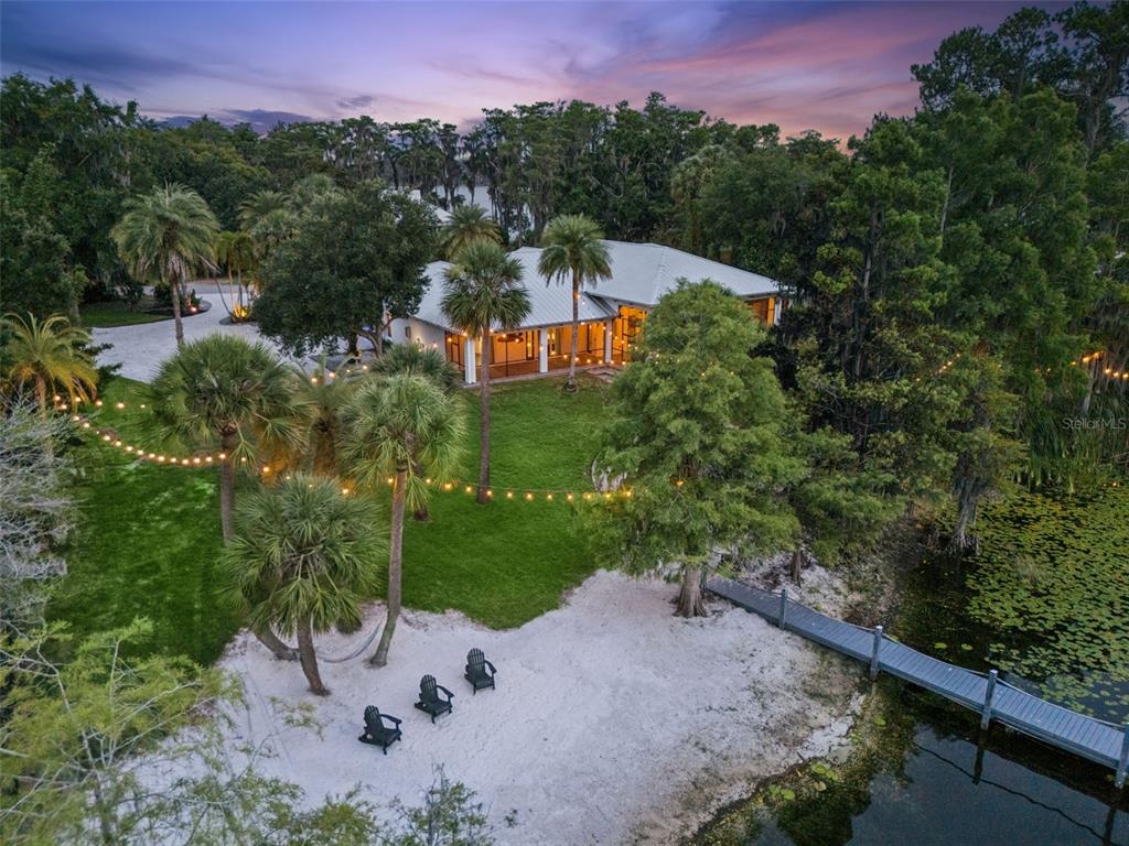 An aerial view of a waterfront house with a sandy beach, dock, and string lights — 5624 W LAKE BUTLER ROAD, WINDERMERE, FL