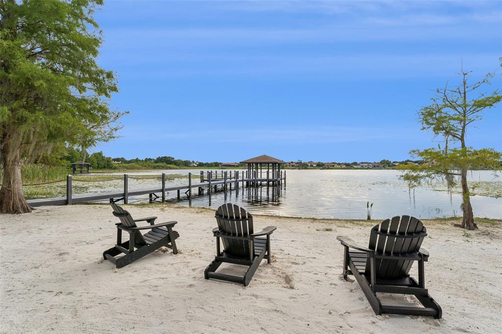 Three black Adirondack chairs sit on a sandy beach overlooking a lake with a dock — 5624 W LAKE BUTLER ROAD, WINDERMERE, FL