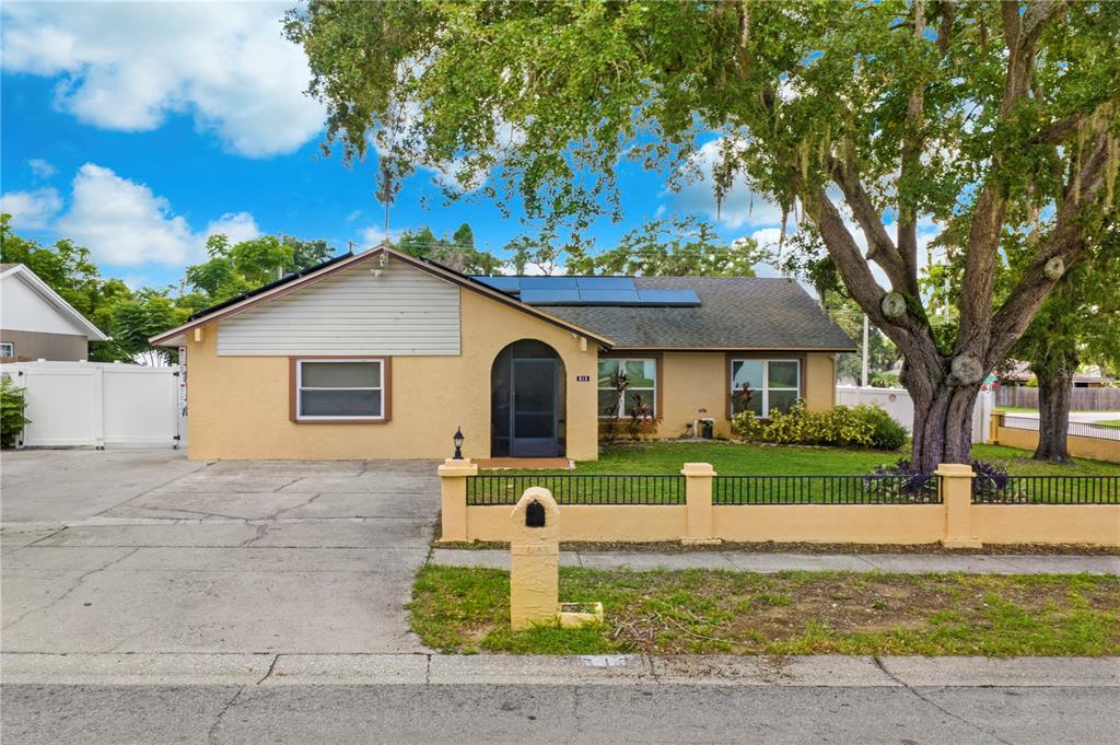 A single-story yellow house with a concrete driveway, arched entryway, and solar panels on roof — 613 FOREST HILLS DRIVE, BRANDON, FL