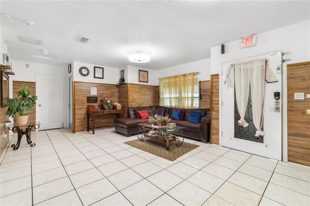 A living room features white tile floors, wood-paneled walls, a brown sectional, and an exit — 613 FOREST HILLS DRIVE, BRANDON, FL