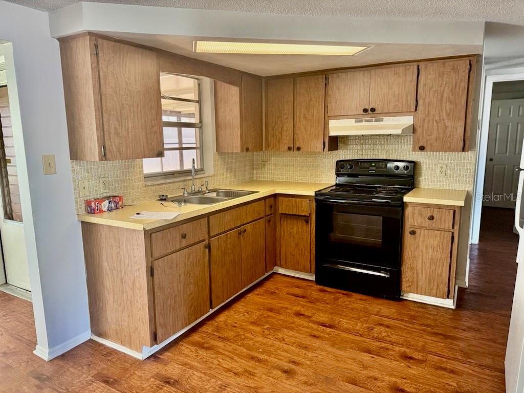 A kitchen with wood cabinets, laminate countertops, a black stove, and wood-look flooring — 9617 LAKE CHRISE LANE, PORT RICHEY, FL