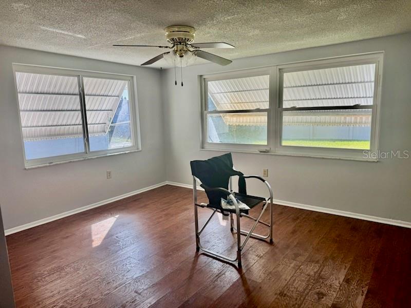 An empty room features wood-look flooring, a ceiling fan, and windows with exterior metal awnings — 9617 LAKE CHRISE LANE, PORT RICHEY, FL