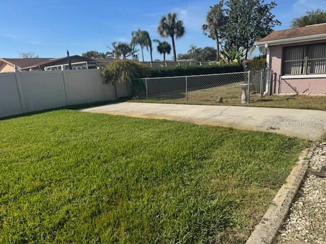 A backyard features a green lawn, a concrete patio, and a white privacy fence — 9617 LAKE CHRISE LANE, PORT RICHEY, FL