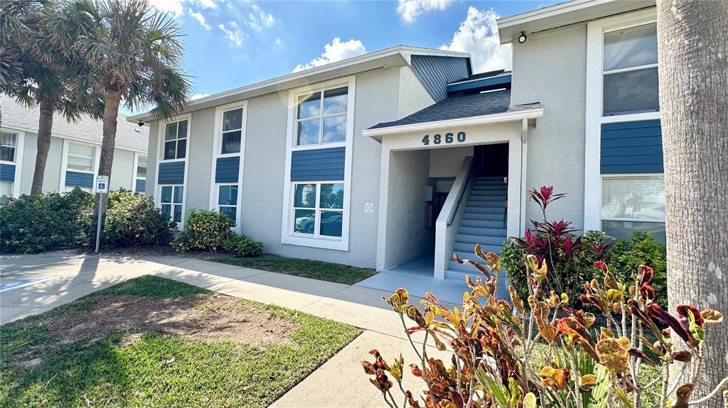 A two-story apartment building exterior features light-colored stucco walls, blue accents, and a concrete staircase — 4860 S ATLANTIC AVENUE UNIT 1030, NEW SMYRNA BEACH, FL