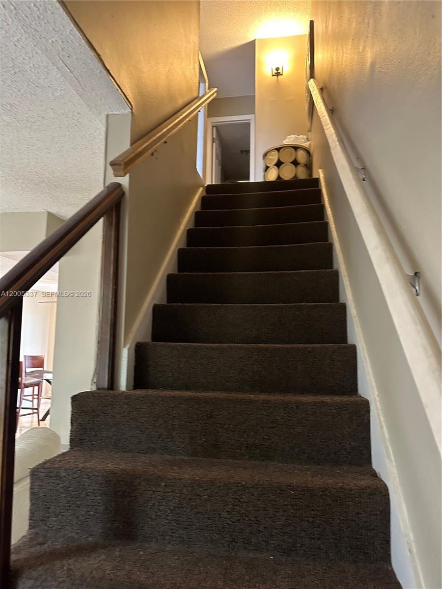 A staircase with dark brown carpeting leads upward between two beige walls — 1100 SE 4th Ave # 32, Deerfield Beach FL 33441, DEERFIELD BEACH, FL