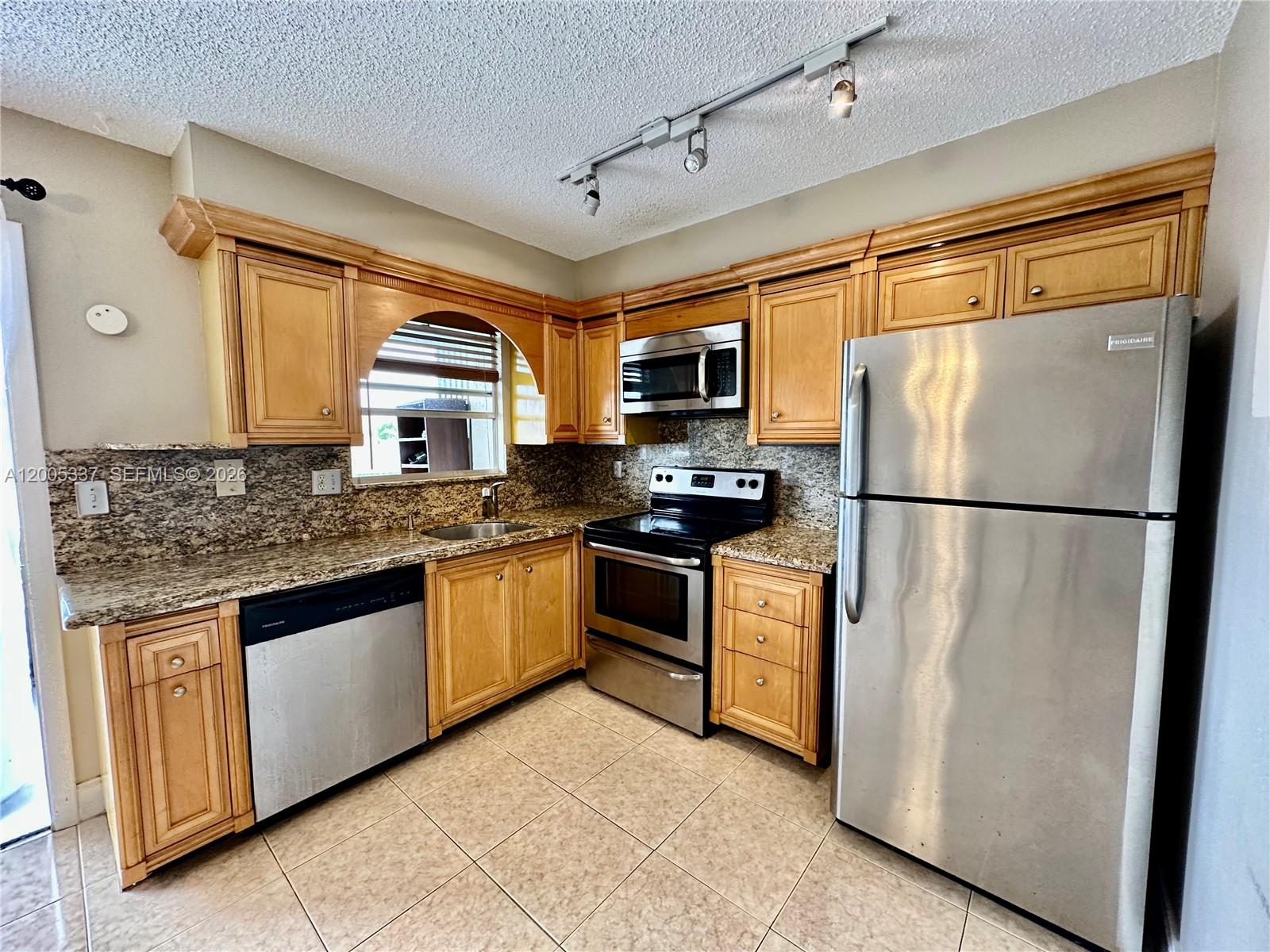 A kitchen features light wood cabinets, stainless steel appliances, granite countertops, and tile flooring — 1100 SE 4th Ave # 32, Deerfield Beach FL 33441, DEERFIELD BEACH, FL