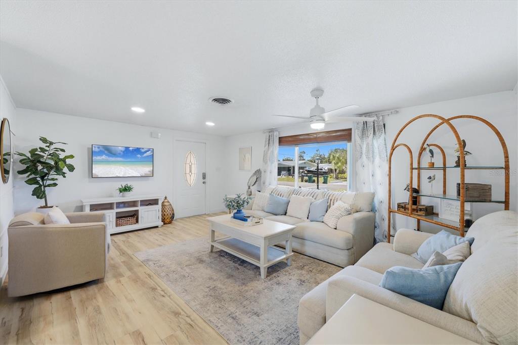 A bright living room features light wood flooring, neutral furniture, and a large window — 1730 BLUE BIRD LANE, ENGLEWOOD, FL