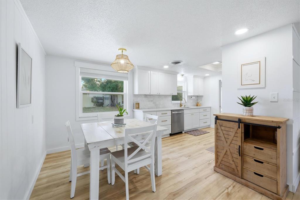 A bright kitchen and dining area features white cabinets, wood-look flooring, and a rustic sideboard — 1730 BLUE BIRD LANE, ENGLEWOOD, FL