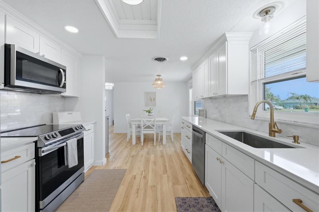A bright kitchen features white cabinets, stainless steel appliances, and a dining area beyond — 1730 BLUE BIRD LANE, ENGLEWOOD, FL