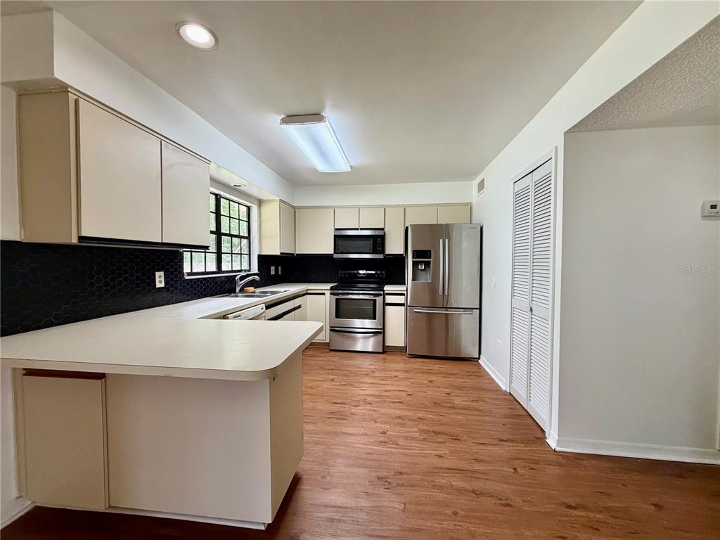 A kitchen features light-colored cabinets, stainless steel appliances, a black backsplash, and wood-look flooring — 2135 BALBOA WAY, KISSIMMEE, FL