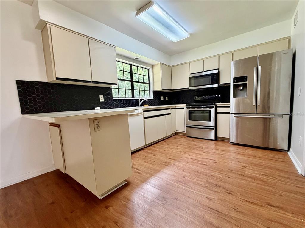 A kitchen features light-colored cabinets, stainless steel appliances, a black honeycomb backsplash, and wood-look flooring — 2135 BALBOA WAY, KISSIMMEE, FL