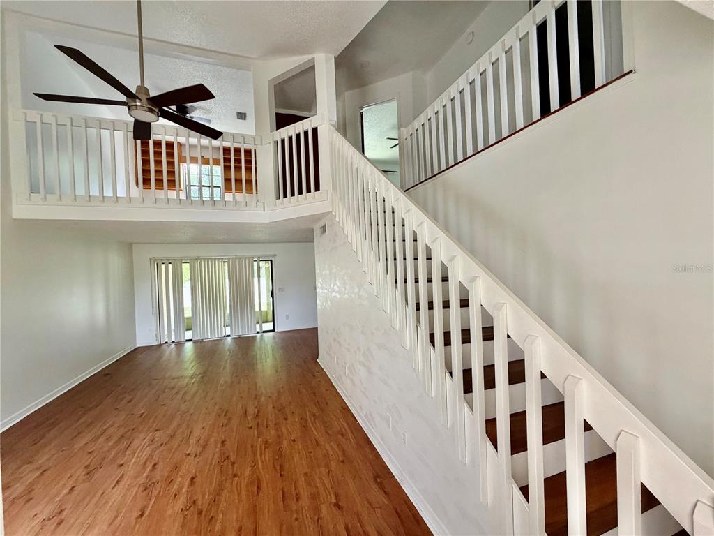 A living room with wood-look flooring, a ceiling fan, and a staircase with white railings — 2135 BALBOA WAY, KISSIMMEE, FL