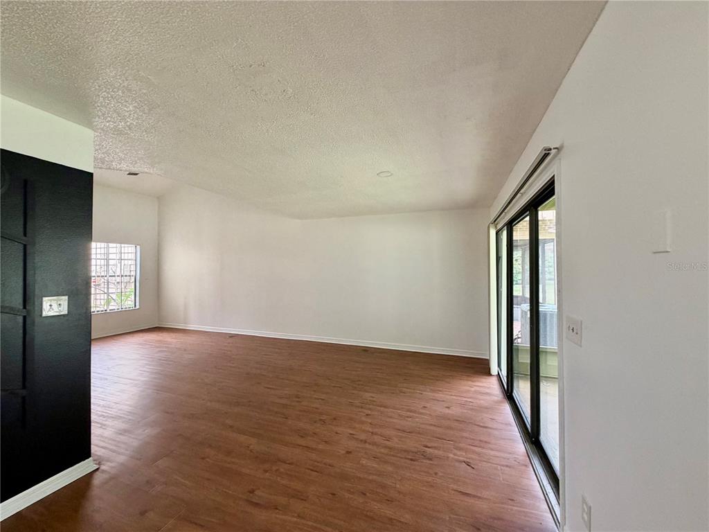 An empty living room features wood-look flooring, white walls, and sliding glass doors — 2135 BALBOA WAY, KISSIMMEE, FL